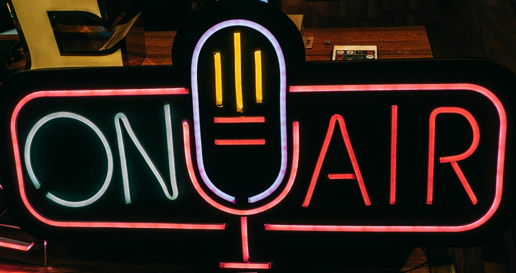 pexels-photo-7317291-7317291 Bright neon 'On Air' sign glowing in a dark studio, perfect for broadcasting themes.